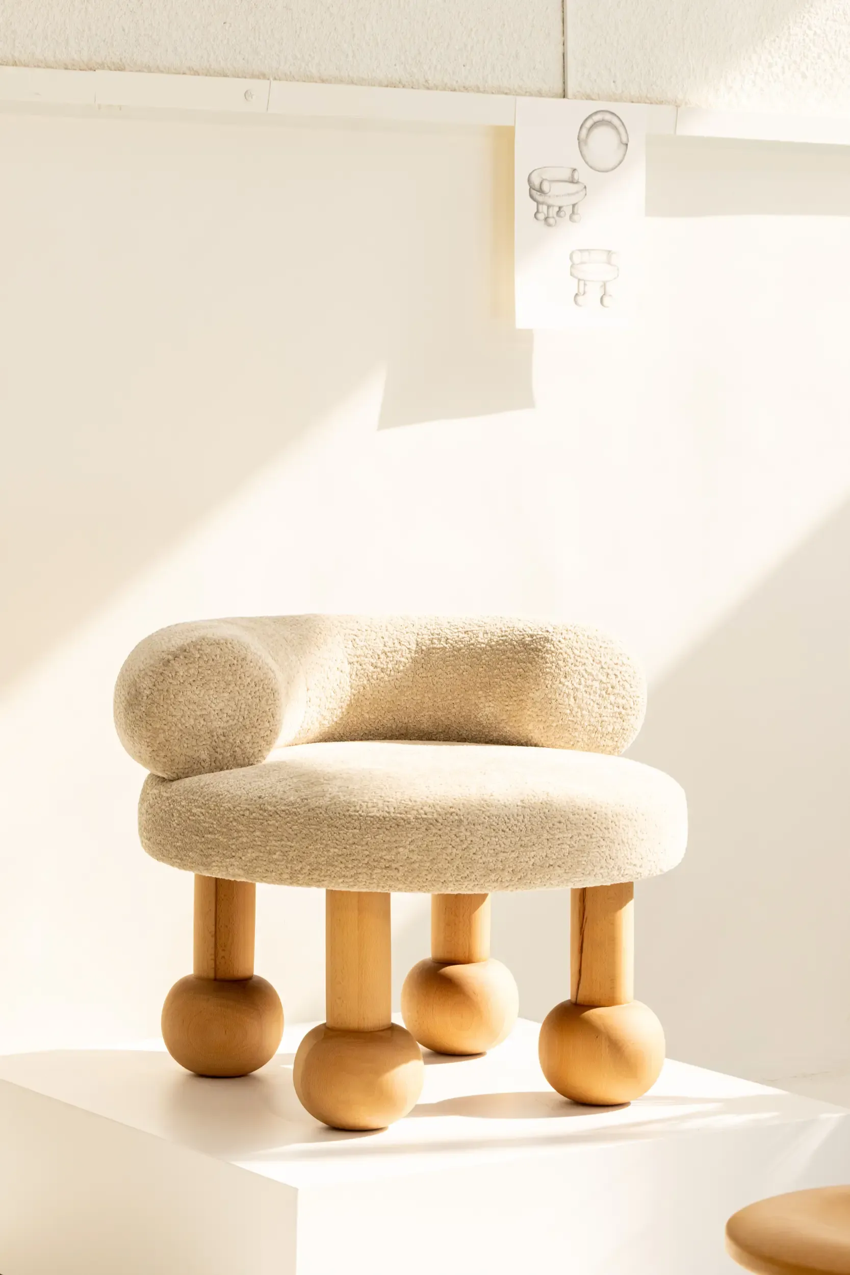 A cream upholstered sculptural chair in a pale interior with angled sunlight.