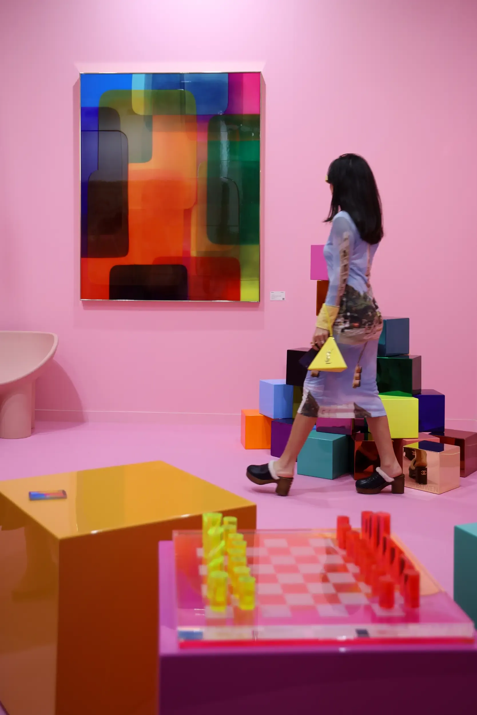 A visitor walking through a vivid pink display of colourful art and design objects.