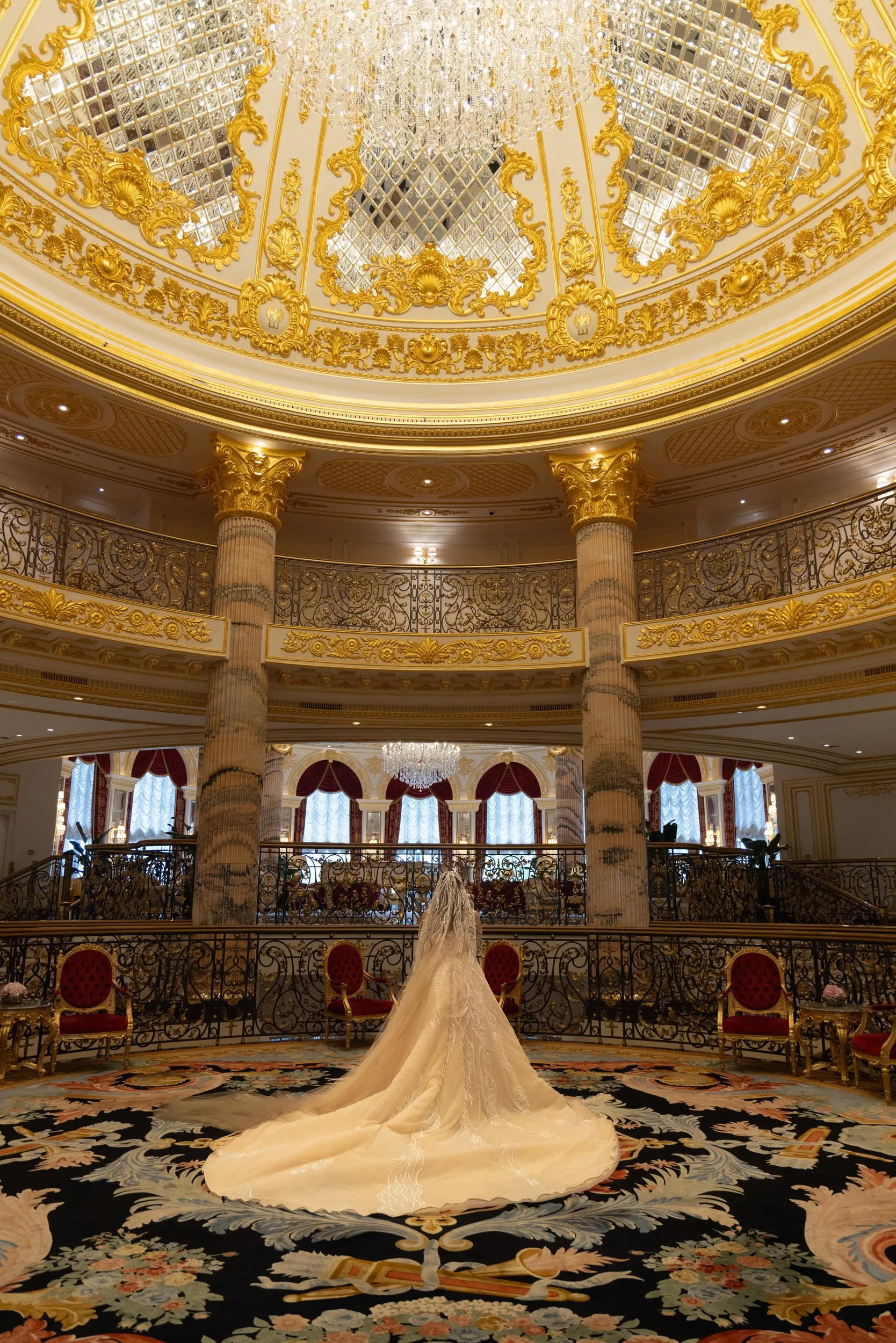 A bride beneath a large crystal chandelier in an ornate circular interior.