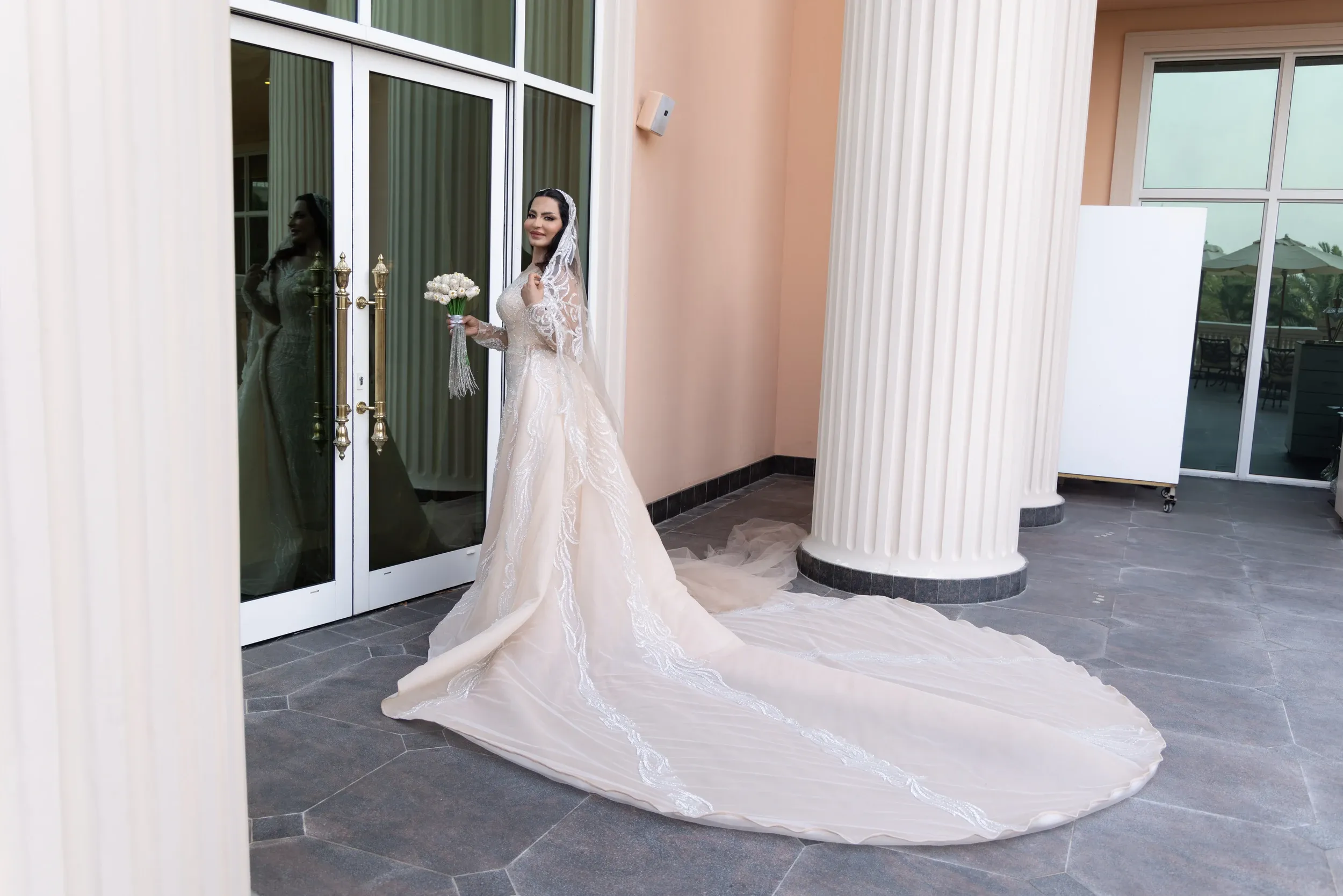 A bride with a long train framed by pale columns and a doorway.