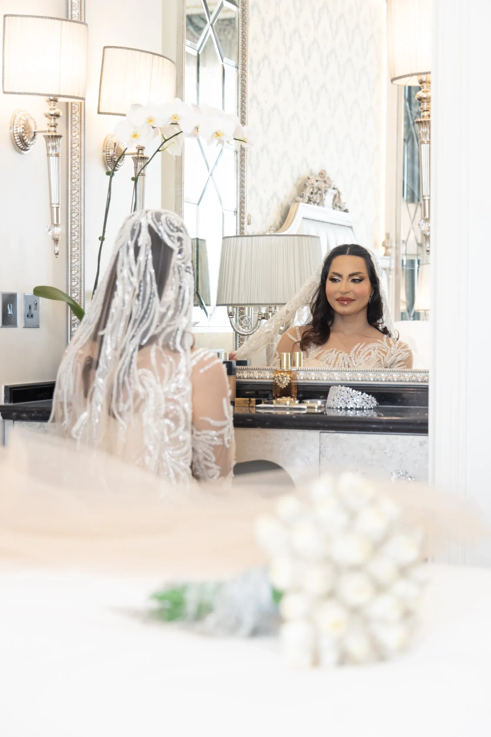 A bride reflected in a dressing-table mirror with a bouquet blurred in the foreground.