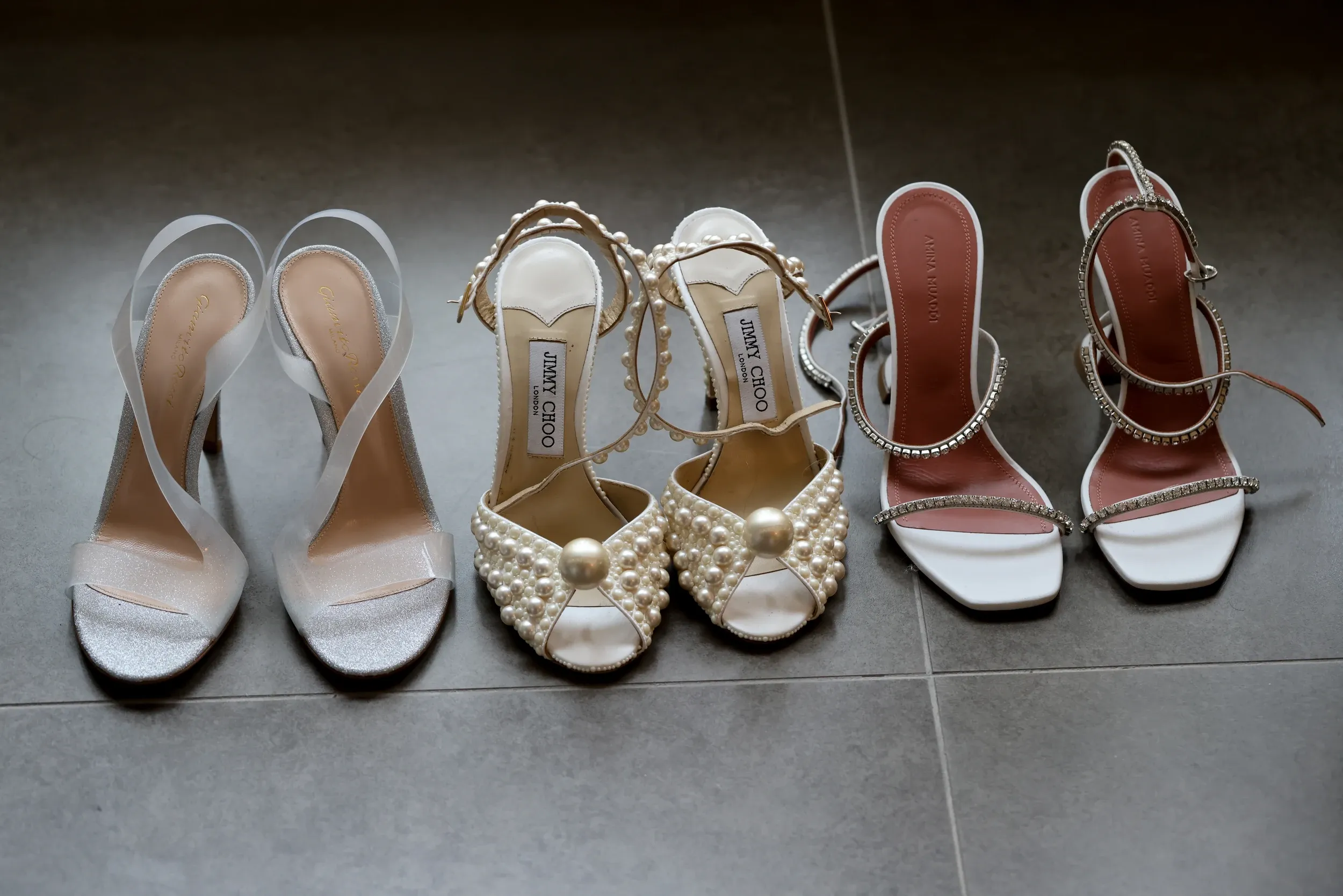 Three pairs of pale bridal shoes arranged on a tiled floor.