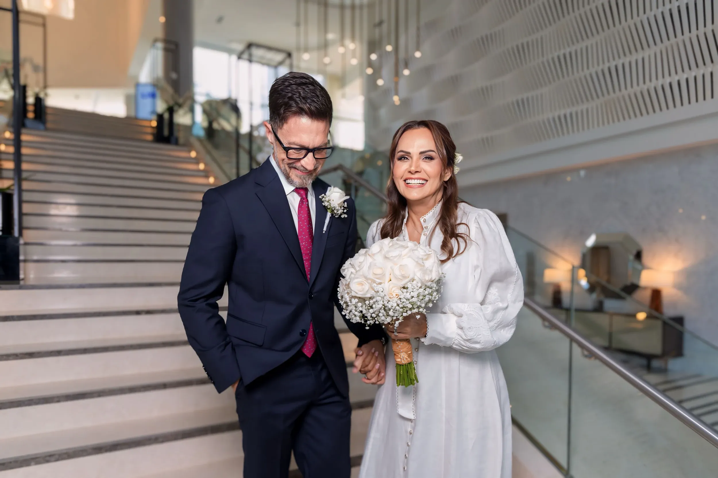 A wedding couple standing together beside a broad interior staircase.